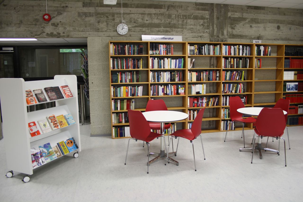 Bilde frå biblioteket, med to bord og stolar og bokhyller.