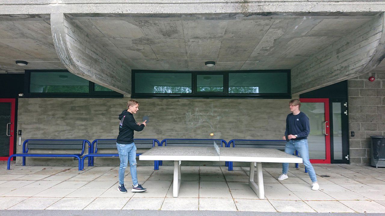 To gutar som speler bordtennis utanfør skulebygget