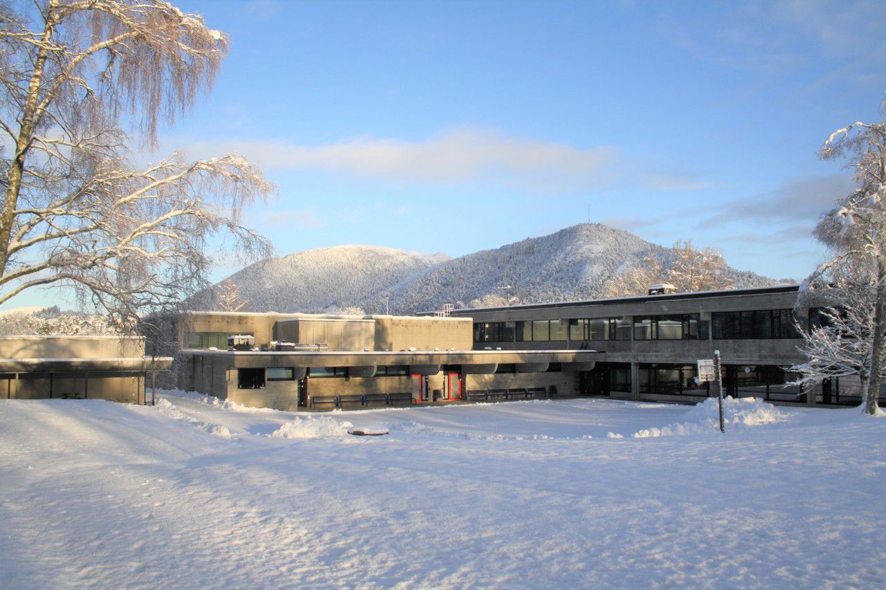 Bilde av skulen og plassen bak skulen, det er snø på bakken og blå himmel, utsikt mot Borgafjellet og Møsnuken.