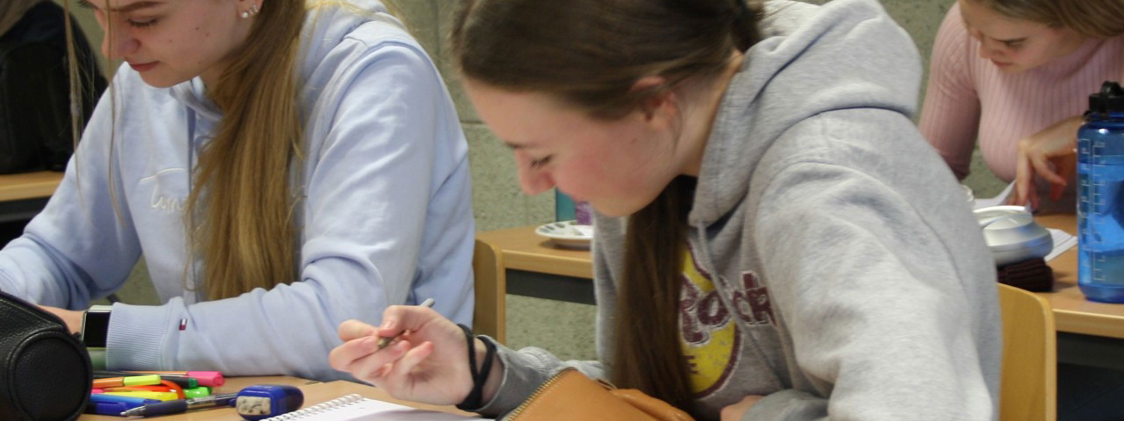 Bilde viser to jenter som sit ved pulten i klasserommet og skriv på PC.