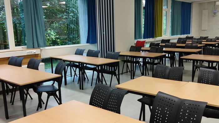 bilde viser et tomt klasserom med pulter og stoler på rekke